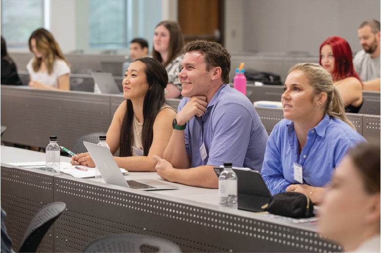 Three students smiling while sitting in lecture hall during orientation watching the front of the classroom